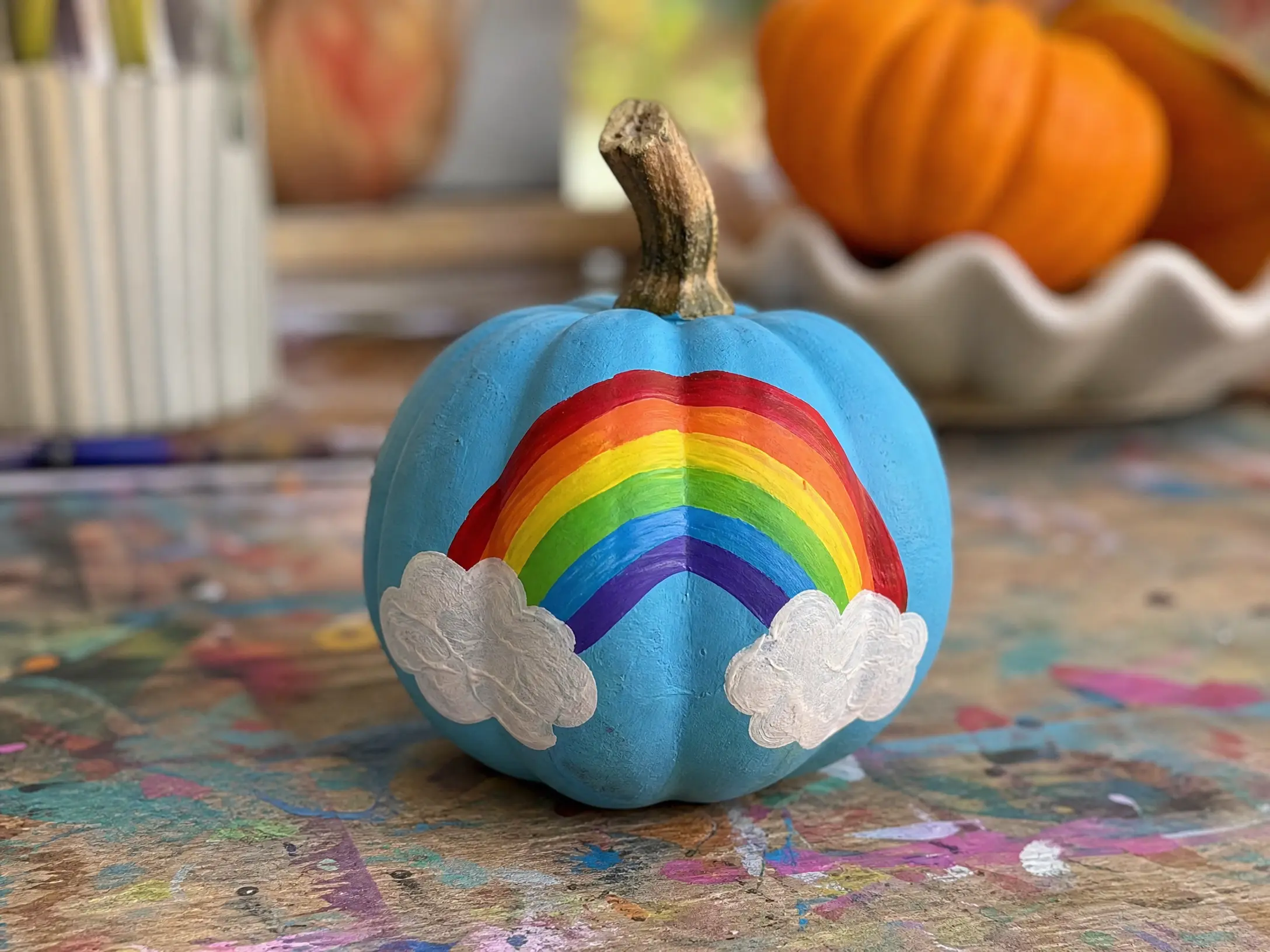 Blue mini pumpkin painted with a rainbow and fluffy white clouds